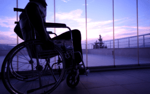 Osoba siedząca na wózku inwalidzkim spogląda przez okno.