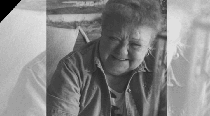 Starsza kobieta siedzi przy stole z lampką wina.