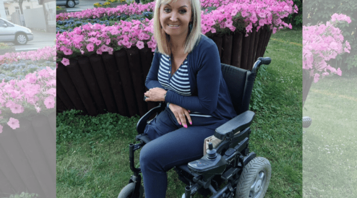 Kobieta na wózku inwalidzkim siedzi przed kwiatami.