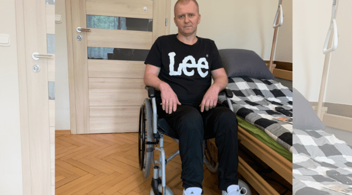 Mężczyzna na wózku inwalidzkim siedzącym przed łóżkiem.