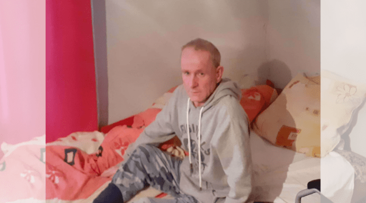 Mężczyzna w szarej bluzy z kapturem siedzącym na łóżku.