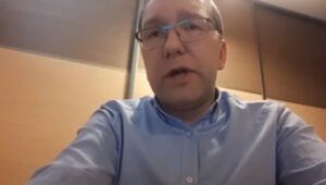 Mężczyzna noszący okulary i niebieską koszulę siedzi przy stole.