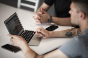 Dwóch mężczyzn siedzących przy stole z laptopami.