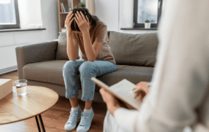 Kobieta siedząca na kanapie z głową w dłoniach.