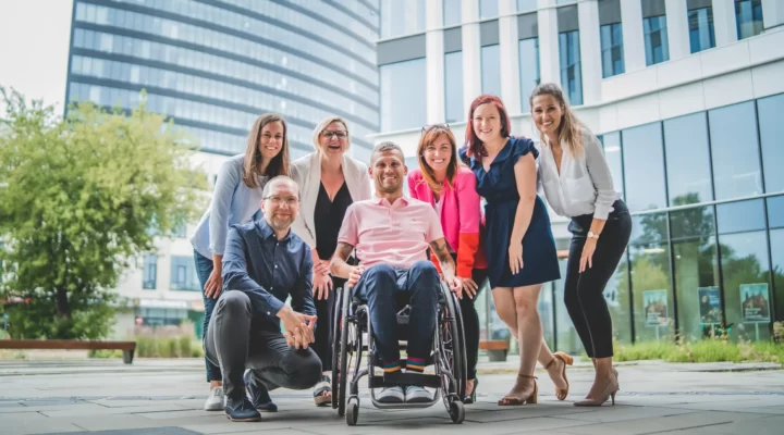 Grupa ludzi pozujących na zdjęcie z kobietą na wózku inwalidzkim.