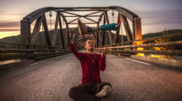 Mężczyzna siedzący na moście z rękami w powietrzu.