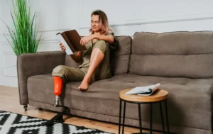 Kobieta z protetyczną nogą siedzącą na kanapie czytając książkę.