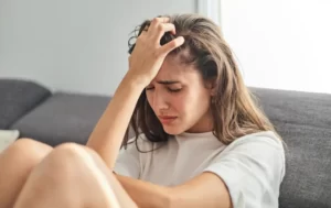 Kobieta siedząca na kanapie z głową w dłoniach.